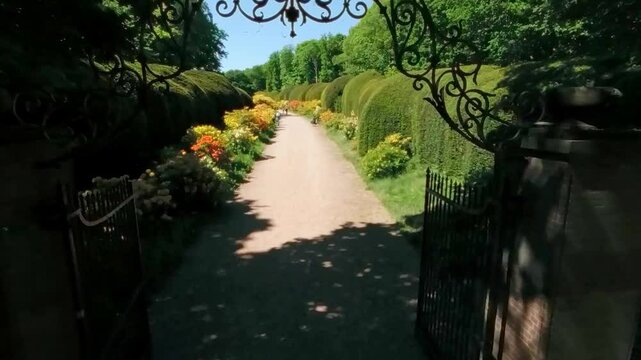 Ornate wrought iron gate opens to a bright garden path lined with flowering bushes and hedges. Location: Heveadorp, Netherlands, Gelderland