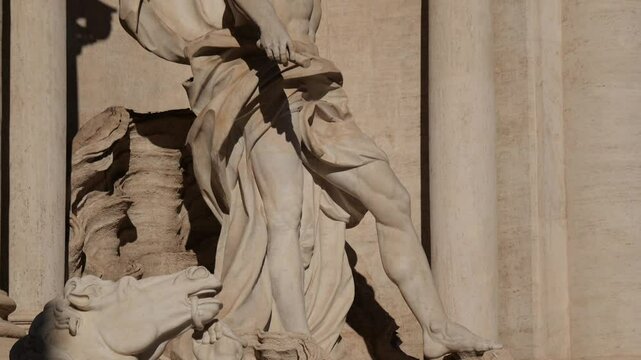 Tilt up on the Oceanus statue at Rome&rsquo;s Trevi Fountain, starting from the feet and rising to the upper torso and head, highlighting dynamic baroque sculpting in sunlight.