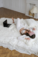 Young female freelancer taking a peaceful nap on her bed with open laptop nearby, illustrating modern remote work challenges and work-life balance. Perfect for concepts of digital nomad lifestyle, wor