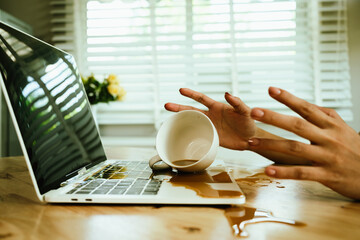 Morning mishap: hot coffee spills over office laptop and documents on a desk, causing wet stains,...