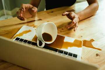 Morning mishap: hot coffee spills over office laptop and documents on a desk, causing wet stains,...