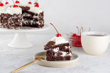 Piece of vegan brownie cake, Black forest or Schwarzwald dessert with chocolate biscuit , cream and cherries with cup of chicory on a white table. Healthy dessert. Sugar, lactose and gluten free.