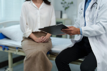 Obraz premium Doctor holding clipboard sitting next to patient on hospital bed