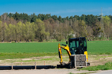 Small excavator working on land preparation near green fields