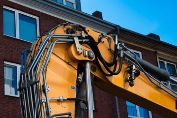 Excavator machinery working near urban building under blue sky