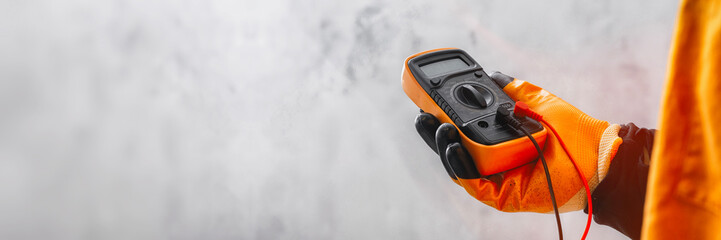 Electrician wearing a protective glove, holding a digital multimeter. Orange colored instrument...