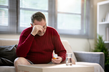 An elderly man is sitting and taking medicine in his home