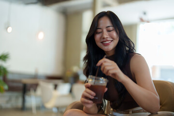 Smiling young woman enjoying iced coffee in a modern cafe