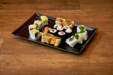 A black plate with a variety of sushi on it. The sushi includes a roll with avocado and a roll with tuna