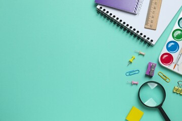 Various colorful school supplies including notebook, magnifying glass and a paints placed neatly on a color background, top view, space for text