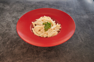 A red plate with pasta and parsley on top. The pasta is white and the parsley is green