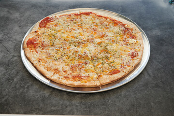 A pizza with cheese and pepperoni on a silver pan. The pizza is cut into slices