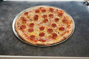 A large pepperoni pizza sits on a metal pan. The pizza is covered in pepperoni and cheese