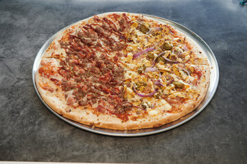A pizza with two different toppings on it. One side has sausage and onions, and the other side has ham and cheese