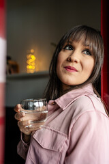 Thoughtful woman drinking water and looking away indoors