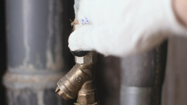 Skilled plumber wearing protective glove confidently shuts off cold water supply at industrial riser using sturdy black valve handle.