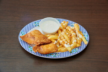 A plate of fried chicken and french fries with a blue and white checkered plate. The fries are covered in a white sauce