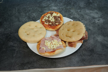 A plate with four different types of food on it. The food is a pizza, a ham sandwich, a ham and cheese sandwich, and a ham and cheese pizza