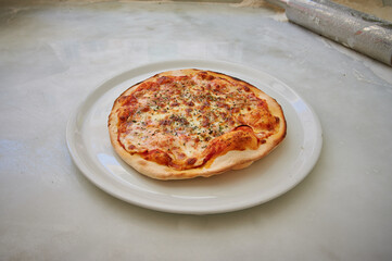 A pizza is sitting on a white plate. The pizza is covered in cheese and has a few toppings