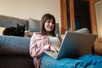 Woman working from home with her cat comfortably sitting on sofa
