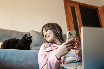 Young woman using smartphone and laptop with her cat at home