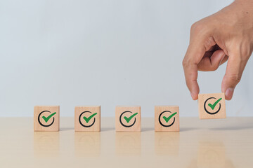 Wooden blocks checklist and green check mark icon with hand on table background. Business task sign...