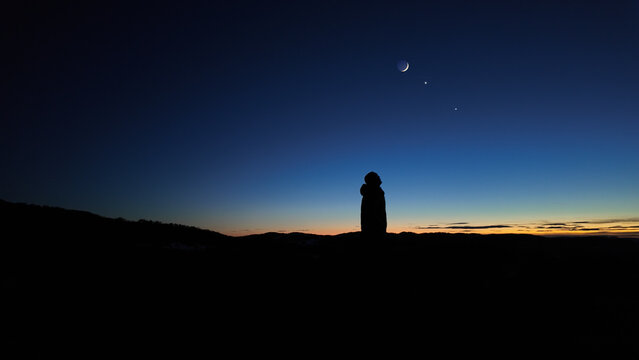 Silhouette of a man observing Milky Way stars, planets and other celestial objects from a dark countryside location.