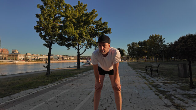 Man taking a break after exercising and jogging in an urban park during sunset hours.