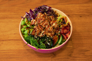 A bowl of food with meat and vegetables. The bowl is pink and has a wooden table underneath it