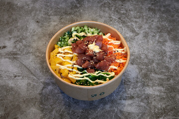 A bowl of food with a green carrot and a yellow carrot. The bowl is made of paper