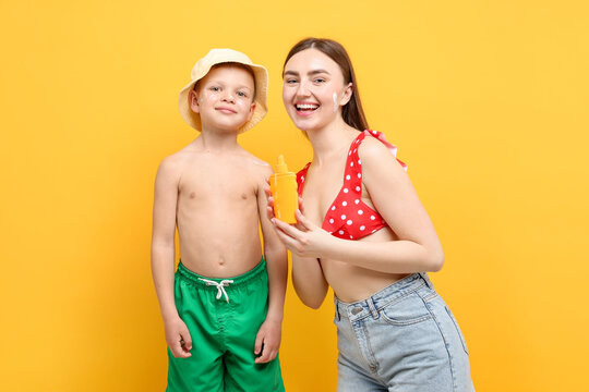 Mother with sun protection cream and her son on yellow background