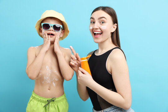Emotional mother with sun protection cream and her son on light blue background - Powered by Adobe