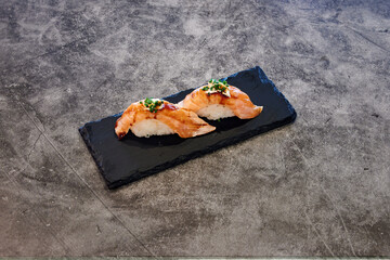 A plate of sushi is placed on a black plate. The sushi is arranged in a way that it looks like a...