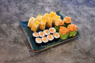 A plate of sushi with a variety of rolls and a side of avocado. The sushi is served on a blue plate
