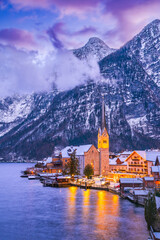 Hallstatt, Austria. Serene Alpine village with snow-covered rooftops on tranquil lake, breathtaking mountain backdrop winter twilight