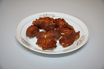 A plate of fried chicken with a gold and white design. There are six pieces of chicken on the plate
