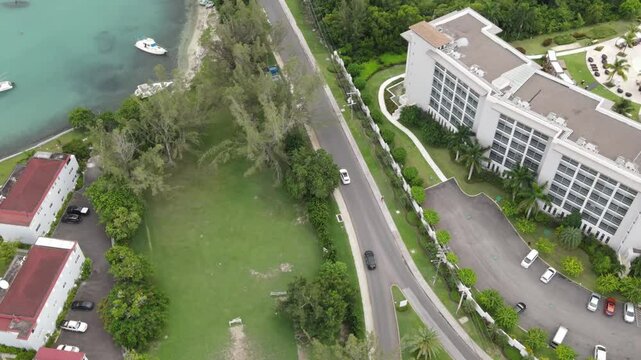Drone footage capturing a sleek car cruising through the upscale community of Freeport, Montego Bay, Jamaica. Lush greenery, ocean views, and luxury villas line the scenic, well-paved road.