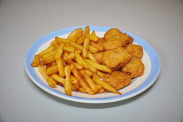 A plate of fried chicken and french fries. The chicken is cut into small pieces and the fries are golden brown