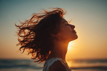 Woman enjoying sunset at the beach with wind blowing through her hair in a serene atmosphere