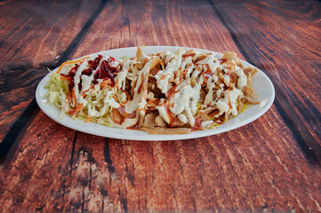 A plate of food with a salad and meat on it. The salad is topped with dressing. The plate is on a wooden table