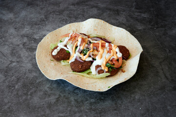 A plate of food with a tortilla wrap and a sauce. The food is made of meatballs and vegetables