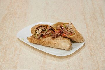 A sandwich is cut in half and placed on a white plate. The sandwich is made with chicken, lettuce, and tomato