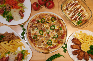 A table with a variety of food including pizza, fries, and chicken wings. There are also several bowls and plates with different types of food