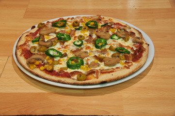 A pizza with mushrooms, olives, and peppers on a white plate. The pizza is sitting on a wooden table