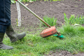 Man in protective clothing mowing grass on path in garden with hand lawn mower. High quality photo