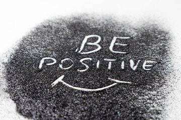 On the black glitters drawing words BE POSITIVE and the smile white background. Abstract minimalist composition from glitter