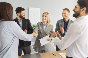 Business people meet for contract negotiation, make a deal, thank each other for collaboration and exchange handshakes. Smiling women shake hands as men applaud. Professional partnership concept