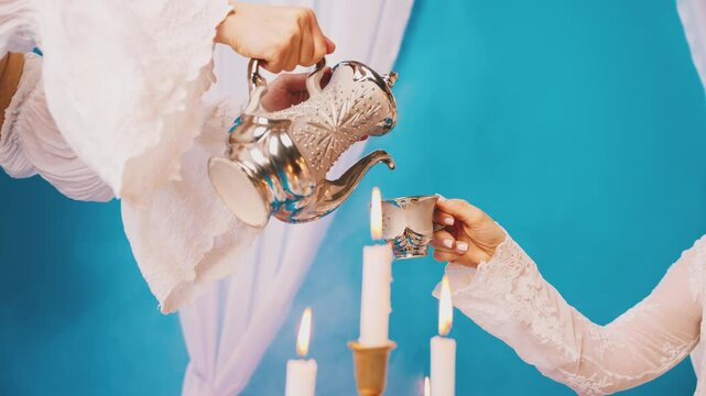 Close-up maid hand pouring tea from teapot into cup of woman queen. Body part lady sitting royal tea party elegant table setting dessert cakes pies. Girl princess style room white lace vintage dress