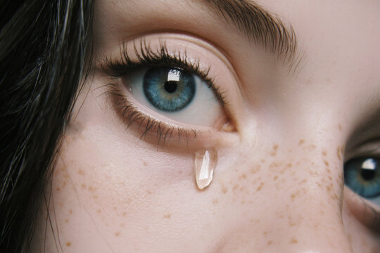 Primer plano detallado del ojo femenino azul llorando, l&aacute;grima visible y expresi&oacute;n emocional profunda, ideal para conceptos de tristeza, sensibilidad y belleza emocional.