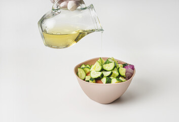 Mixed vegetable salad in a bowl on a white background. A woman's hand poured olive oil on the salad